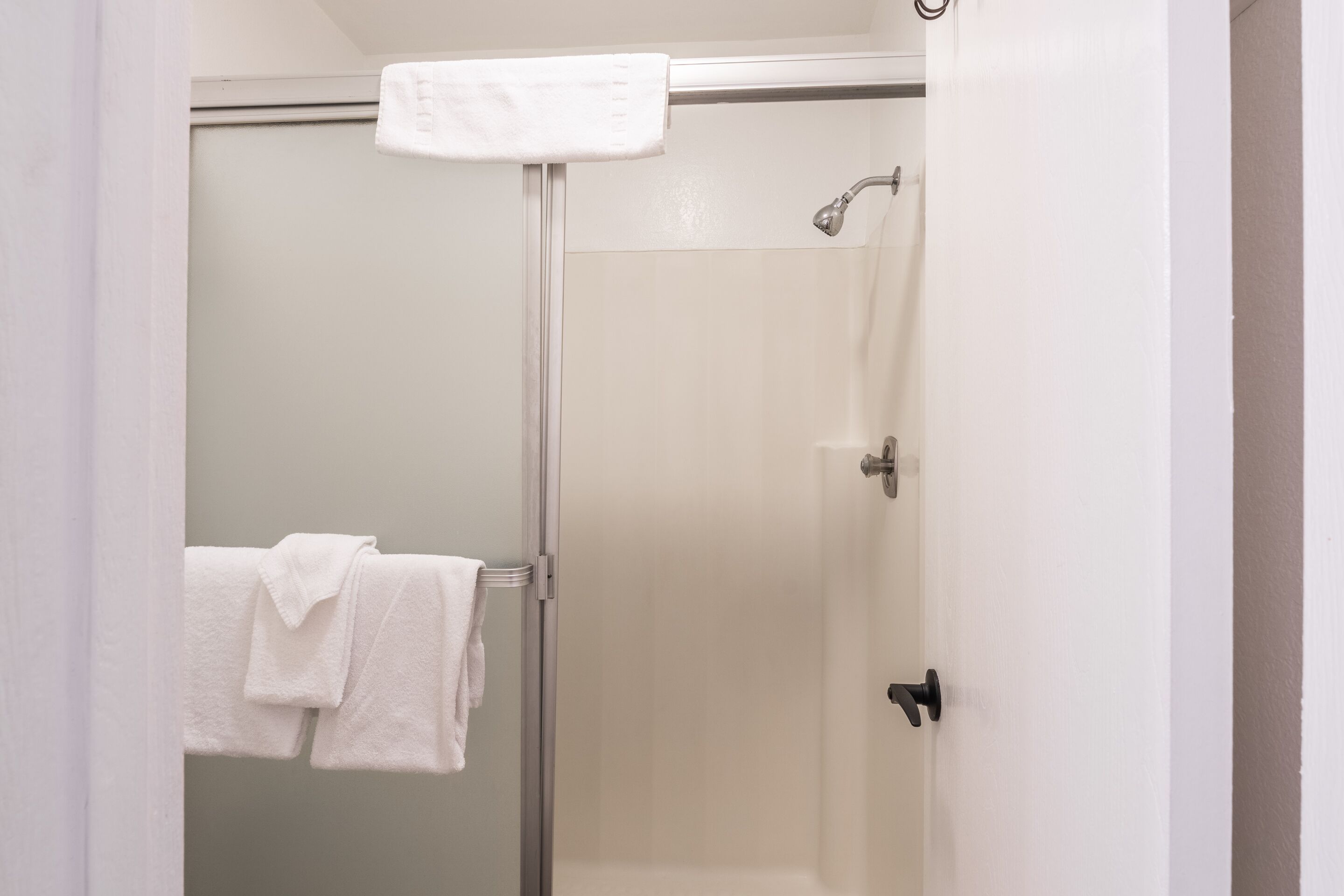 A bathroom with a glass shower enclosure, a white towel hanging on a rack, and a visible showerhead.