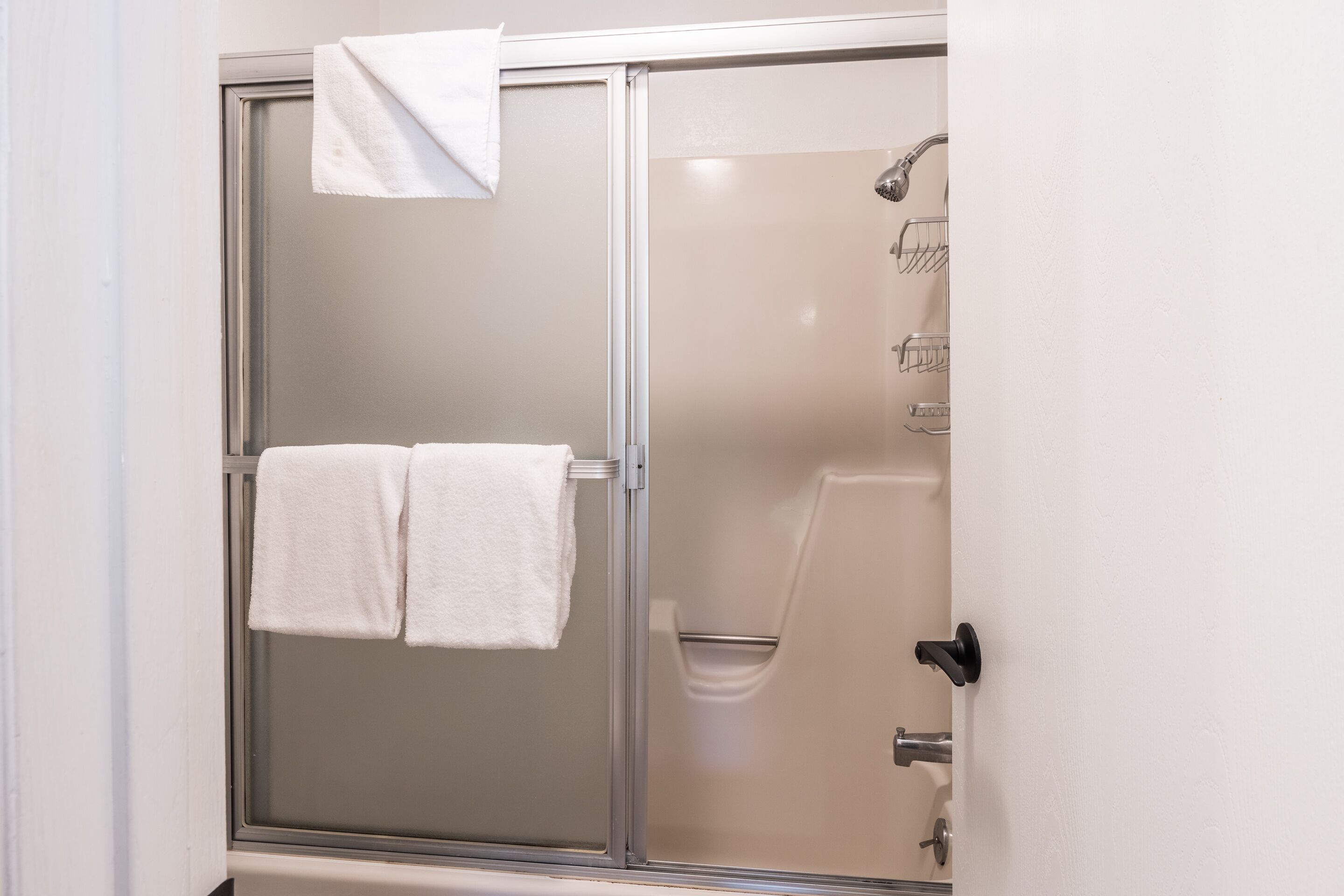 A shower with a glass door, a white towel hanging on the door, and a showerhead.