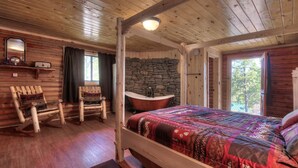 A log cabin bedroom with a four-poster bed, a stone wall, a wooden rocking chair, and a large window.