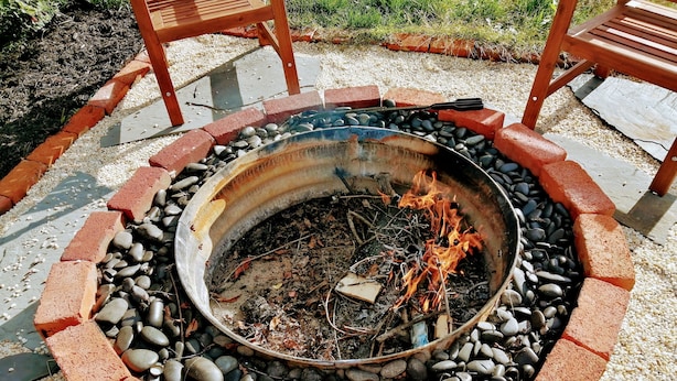 Un foyer circulaire, entouré d’une bordure en briques et de galets, avec des chaises disposées tout autour.