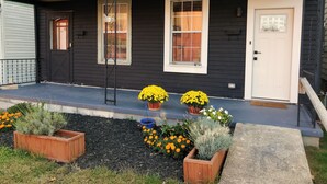 Une maison noire avec un porche, deux fenêtres, une porte et un petit jardin agrémenté de plantes en pot.