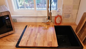Une cuisine dotée d’un plan de travail en bois, d’un four à micro-ondes en acier inoxydable, d’un évier noir et d’une fenêtre donnant sur du mobilier d’extérieur.