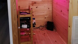 Une pièce chaleureuse aux murs en bois et au plafond en pente, agrémentée d’un néon indiquant « Roseal day » et d’une petite étagère où sont posées des bouteilles de vin.