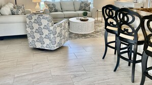 A living room with a sofa, a patterned armchair, a coffee table, and a dining area with chairs. - Beautiful, Spacious Heated Pool Home - Close to Siesta Key Beach! (Sarasota)