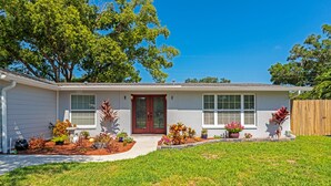 A single-story house with a front porch, a red door, and a small garden with various plants and flowers. - Beautiful, Spacious Heated Pool Home - Close to Siesta Key Beach! (Sarasota)