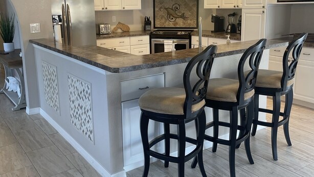 A modern kitchen with white cabinets, a central island with bar stools, stainless steel appliances, and pendant lighting. - Beautiful, Spacious Heated Pool Home - Close to Siesta Key Beach! (Sarasota)