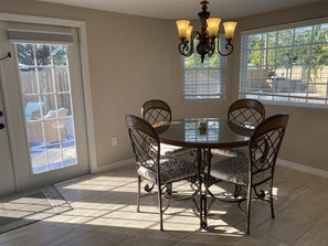 A dining area with a glass table, four chairs, a chandelier, and large windows.