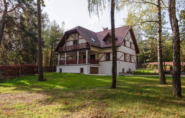 Een huis met twee verdiepingen en een balkon, omringd door bomen en een verzorgd gazon.