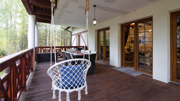 Una terraza de madera con una hamaca colgante, una mesa y vistas al bosque.