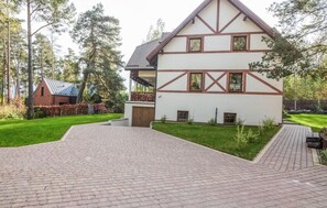 Een woonhuis met twee verdiepingen, een flauw hellend dak, een duidelijke veranda en een verharde oprit naar de ingang.