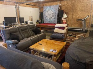 Una sala de estar con mesa de billar, sofá de cuero y caminadora.