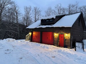 A wooden barn with red garage doors and a snow-covered roof.