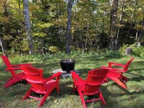 Un camping con un brasero y cuatro sillas Adirondack rojas dispuestas a su alrededor.