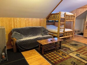 A wooden interior with a bunk bed, a sofa, a small table, and a patterned rug.
