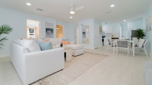 A modern living room with a white sofa, a dining area with a table and chairs, and a kitchen in the background. - Renovated 3bd/2ba near Downtown (West Palm Beach)