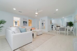 A modern living room with a white sofa, a dining area with a table and chairs, and a kitchen in the background. - Renovated 3bd/2ba near Downtown (West Palm Beach)