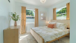 A bedroom with a bed, a bedside table, a lamp, a plant, and a window with curtains. - Renovated 3bd/2ba near Downtown (West Palm Beach)