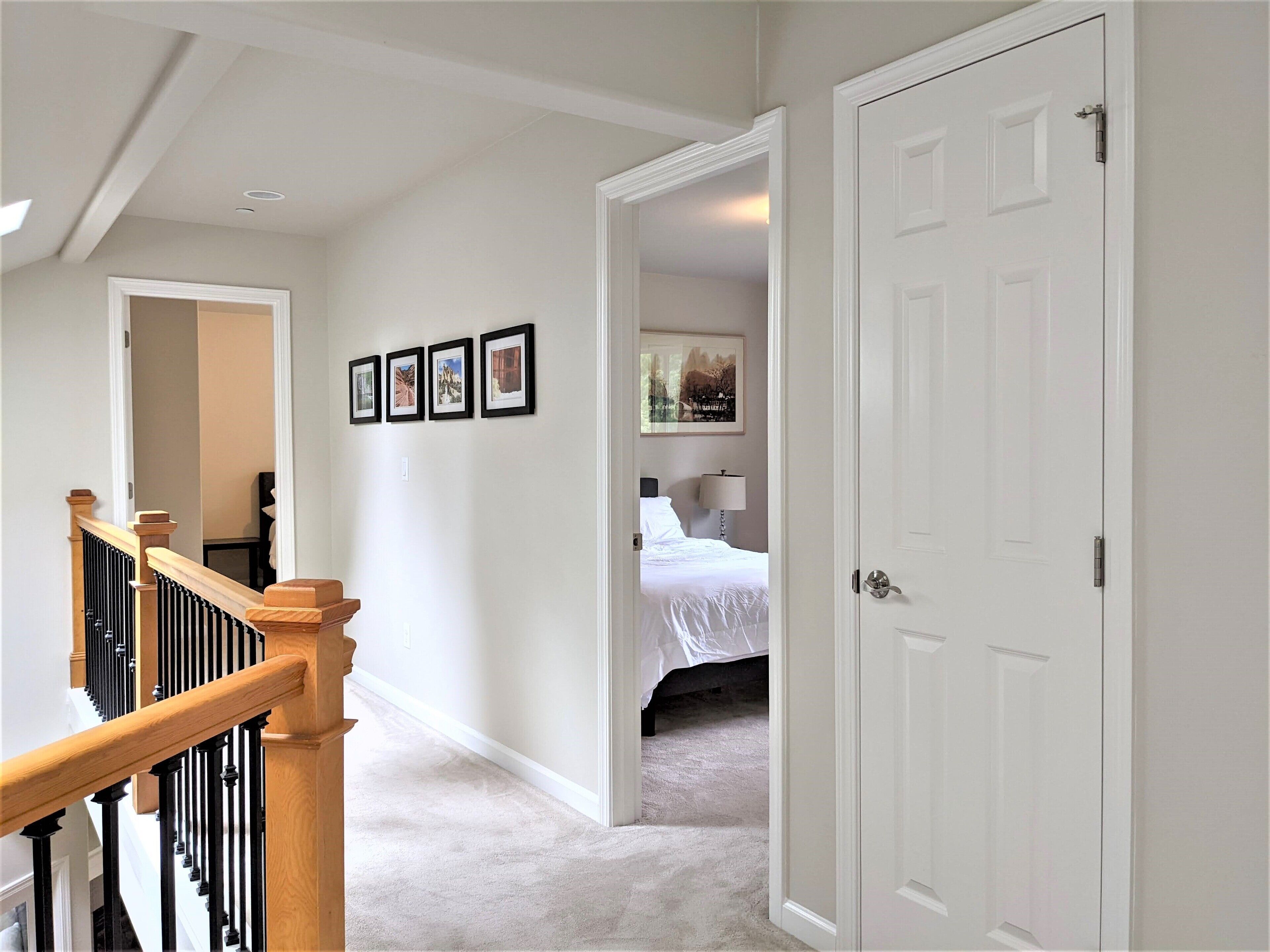 A hallway with a staircase, a bed, and a door.