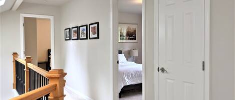 A hallway with a staircase, a bed, and a door.