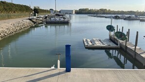 Un port de plaisance avec des bateaux amarrés, une promenade en béton et une étendue d’eau calme.