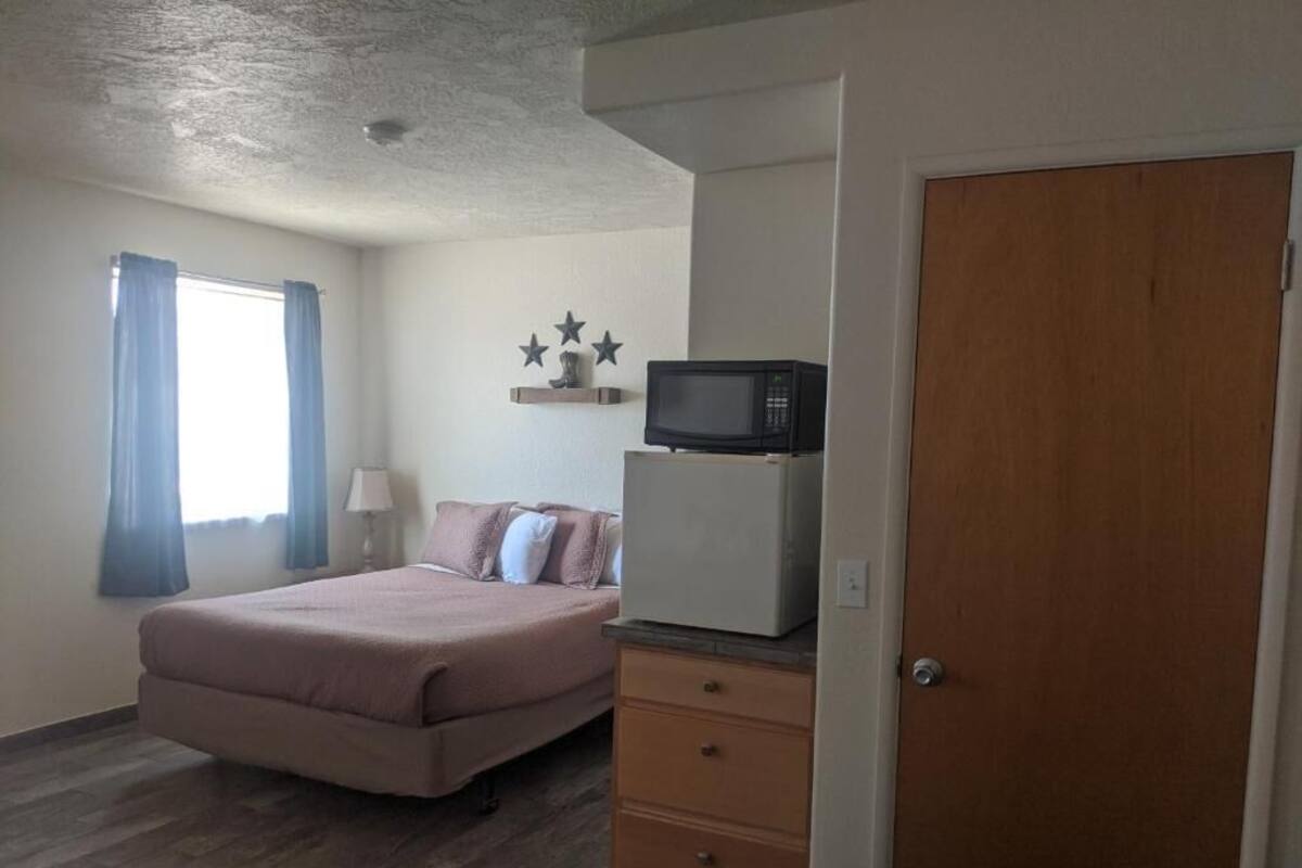 A bedroom with a bed, a dresser, a microwave, and a door.