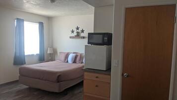 A bedroom with a bed, a dresser, a microwave, and a door.
