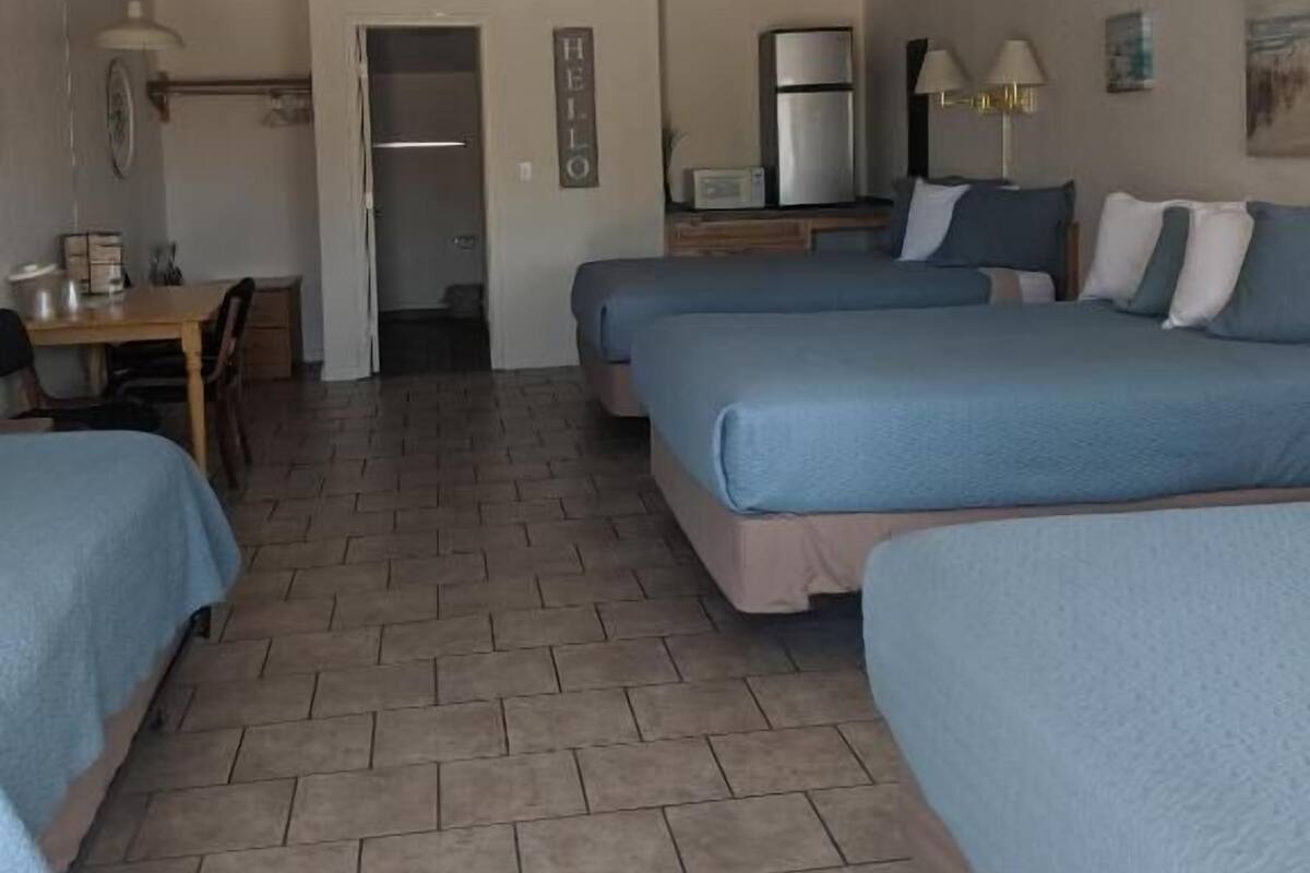 A hotel room with two beds, a kitchenette, a dining area, and a bathroom.