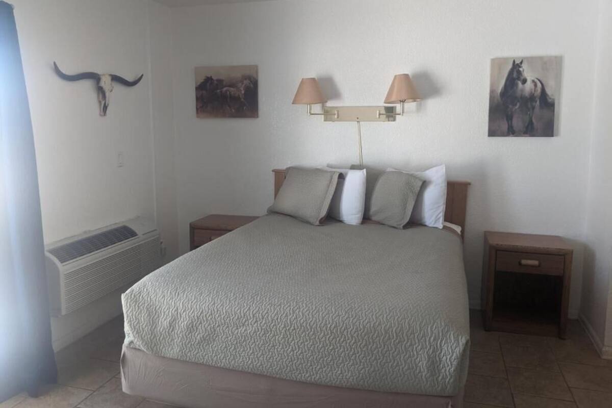 A bedroom with a bed, two bedside tables, a wall-mounted lamp, and a wall-mounted heater.