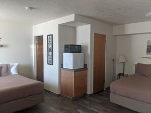A hotel room with two beds, a microwave, a refrigerator, a wooden cabinet, and a door.