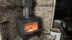 Una chimenea de ladrillo con un estufa de leña moderna, un cubo de metal con leña y una caja con la etiqueta '70 CLB'.