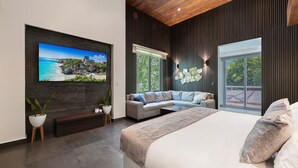 Een moderne slaapkamer met een groot bed, een bank, een aan de muur bevestigde televisie en een balkon met tuinmeubilair.