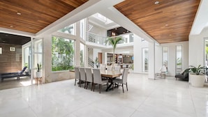 Een ruim, modern interieur met een hoge plafond, een centraal eetgedeelte en grote ramen voor natuurlijk lichtinval.