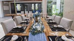 Een eetruimte met een lange tafel gedekt voor een formeel diner, omringd door moderne stoelen, en met een centraal bloemstuk.