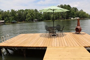 A wooden dock with a table and chairs, a green and white striped umbrella, and a rustic chimney.