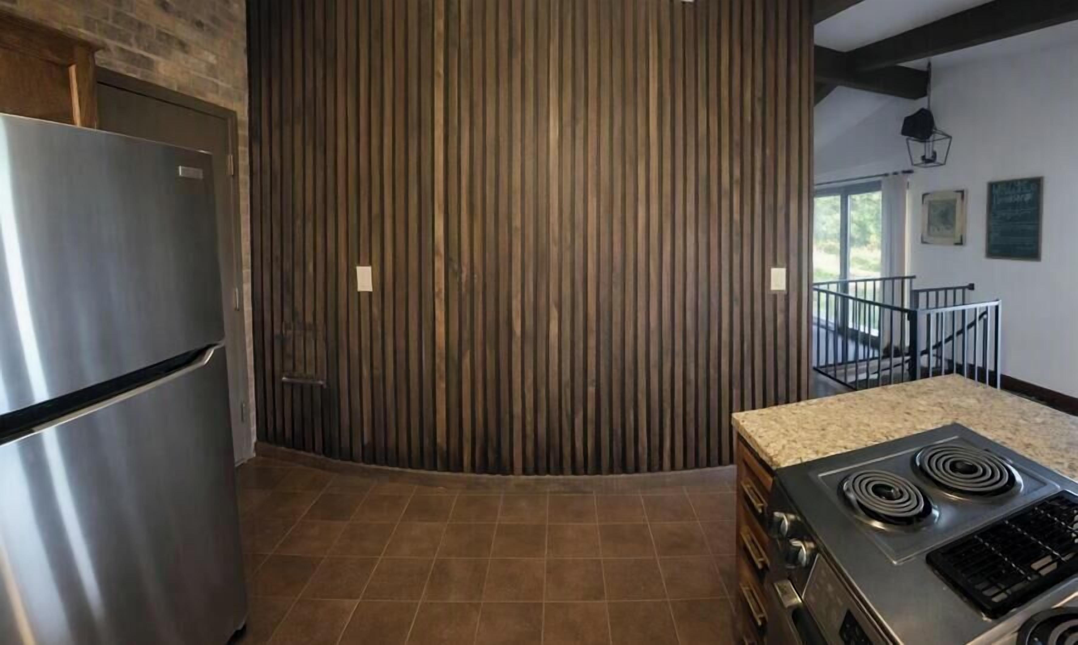 A kitchen with a stainless steel refrigerator, a stove, and a wooden slatted wall.