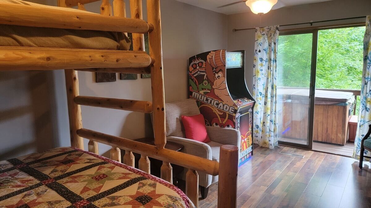 Une chambre avec un lit superposé, un canapé, une console de jeux et une porte-fenêtre coulissante donnant sur un balcon.