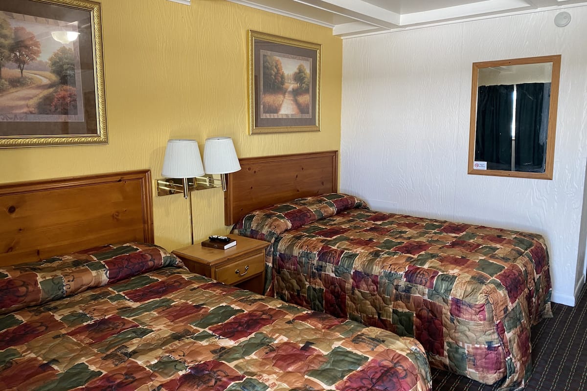 A hotel room with two beds, a nightstand with lamps, and two framed pictures on the walls.
