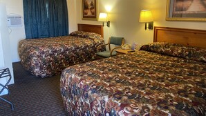 Une chambre d’hôtel avec deux lits, un bureau, une chaise, une lampe et un tableau au mur.