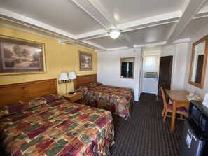 A hotel room with two beds, a desk, a chair, a microwave, and a small refrigerator.