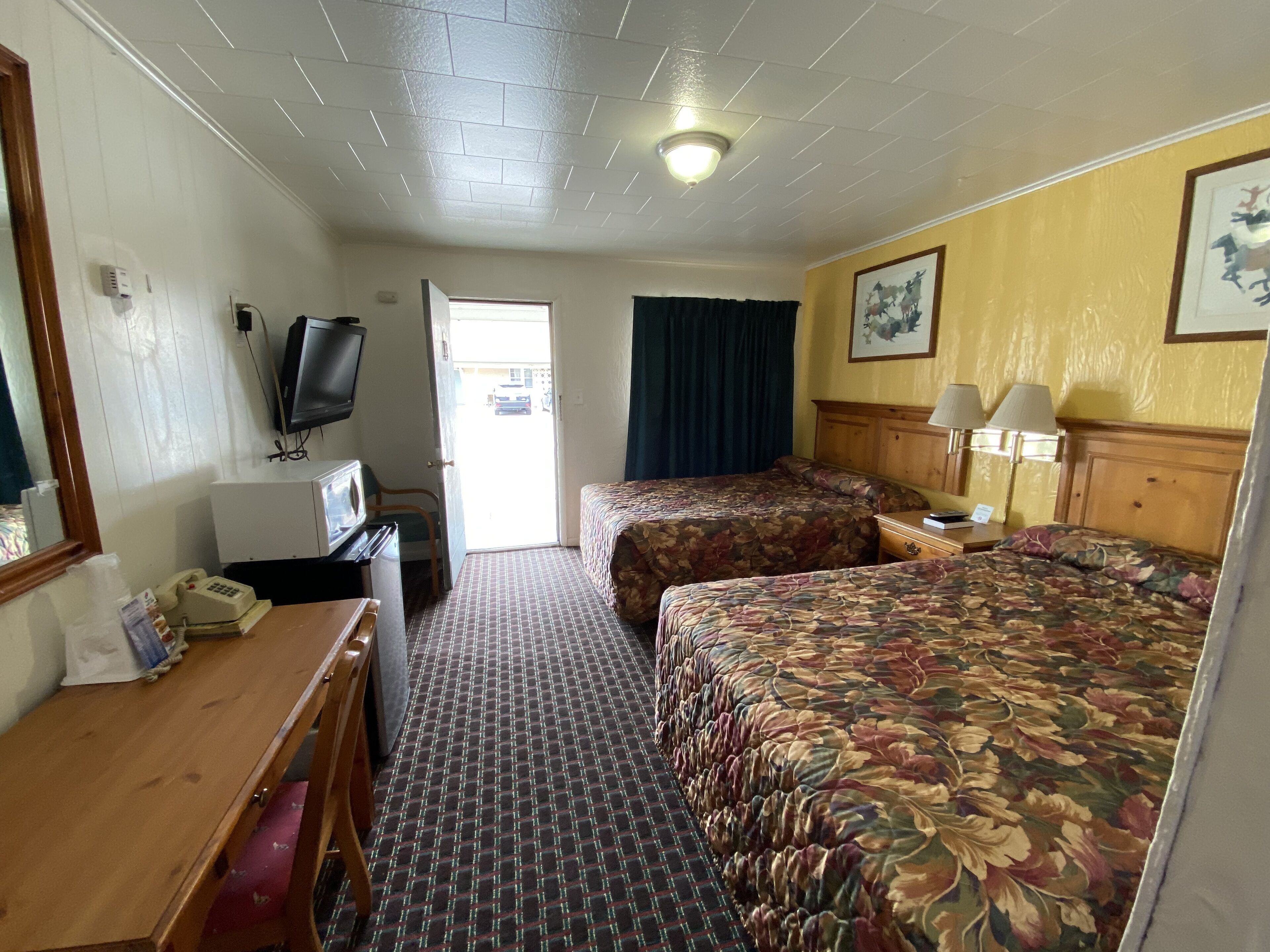 A hotel room with two beds, a desk with a telephone, a television, and a door leading outside.