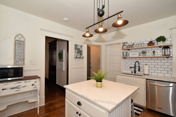 A modern kitchen with white cabinetry, a central island, a stainless steel dishwasher, and pendant lighting.