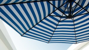 Un espace aménag é au bord de la piscine, avec une table en verre, deux boissons orange, un parasol rayé et des chaises longues blanches.