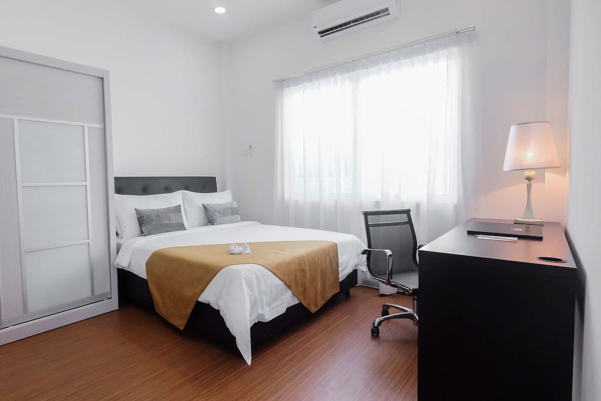 Ein Hotelzimmer mit einem Bett, einem Schreibtisch, einem Stuhl und einem mit Vorhängen versehenen Fenster.