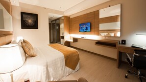 Une chambre d’hôtel avec un lit, un bureau, une chaise et un téléviseur fixé au mur.