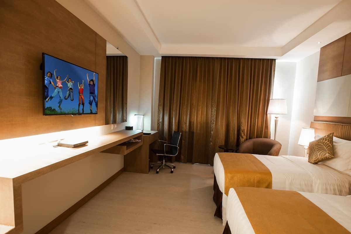 Ein Hotelzimmer mit einem Holztisch, einem Fernseher, einem Bett, einem Sessel und einem Fenster mit Vorhängen.