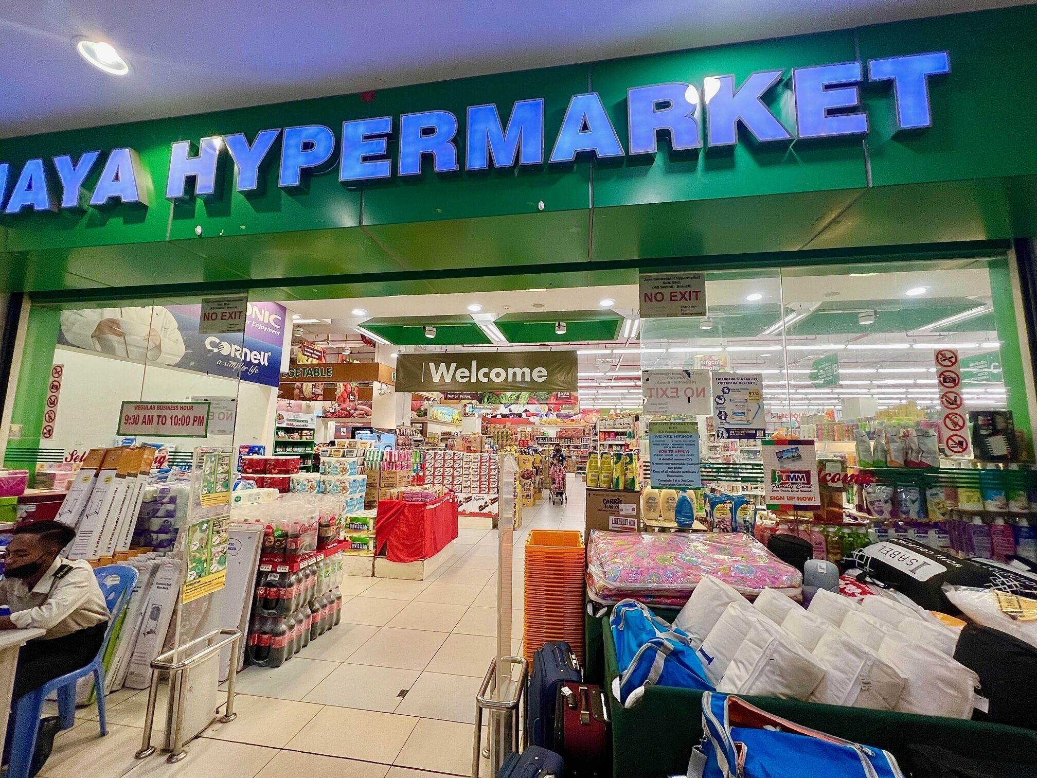 Eingang eines Hypermarktes mit einem 'Welcome'-Schild, verschiedenen Produktpräsentationen und einem 'No Exit'-Schild.