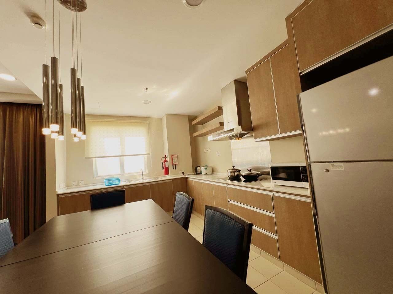 Una cocina moderna con comedor, que incluye electrodomésticos de acero inoxidable, armarios de madera e iluminación colgante.
