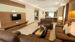 Une chambre d’hôtel moderne dotée d’une télévision à écran plat, de sièges confortables, d’un coin repas et d’une cuisine en arrière-plan.