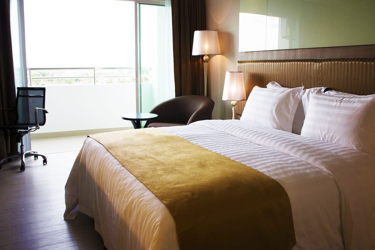 Ein Hotelzimmer mit einem großen Bett, einem Schreibtisch, einem Stuhl und Blick ins Freie.