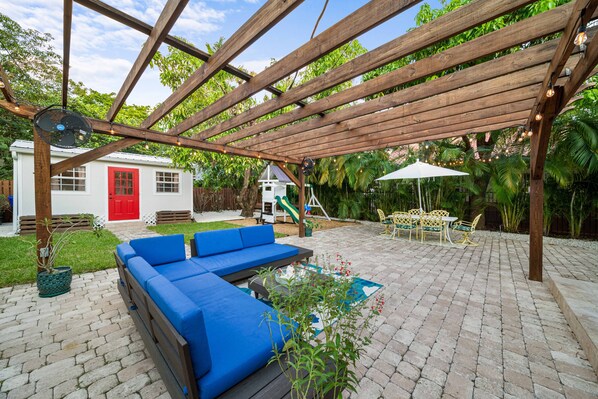 A covered patio with a wooden pergola, outdoor seating, and a small play area.